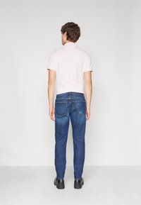 Camisa polo corta de color rosa claro con cuello clásico, combinada con jeans de mezclilla rectos de color azul oscuro y zapatos negros, vista desde la parte posterior.
