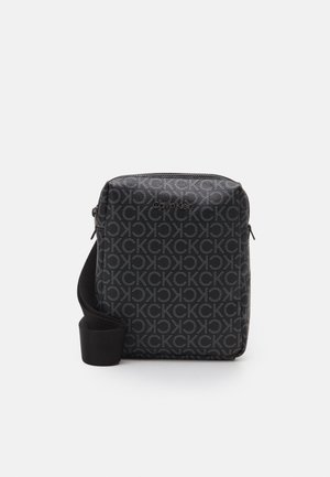 Sac bandoulière noir Calvin Klein avec motif répétitif du logo "CK" et fermeture éclair à l'avant, équipé d'une bandoulière réglable.