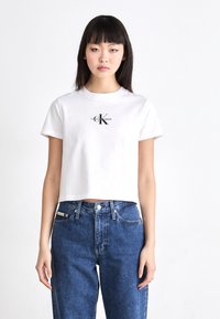 Witte cropped t-shirt van katoen met een ronde halslijn, voorzien van een zwart logo "Calvin Klein Jeans" en korte mouwen. Gepaard met hoge blauwe jeans.