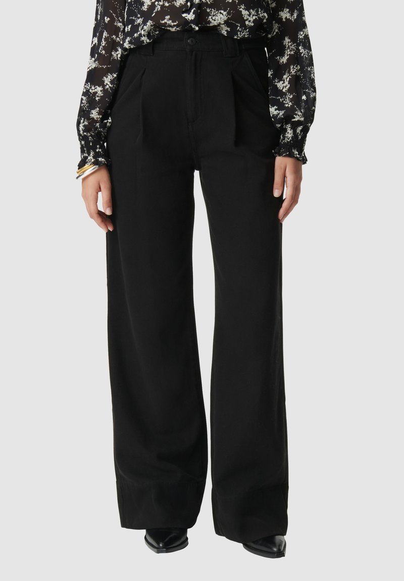Pantalones amplios negros de cintura alta, con pliegues, cierre de botón y una textura suave. Combinados con una blusa de manga larga con estampado floral.