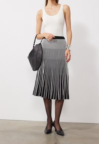 Jupe plissée à rayures verticales noir et blanc, associée à un débardeur crème, un sac en cuir noir, des talons noirs et des collants noirs transparents.