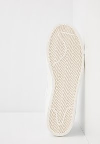 Valkoiset lenkkarit, joissa on herringbone-urituspohja ja teksturoitu pinta. Sivuprofiilissa näkyy sileä päällinen ja pyöristetty varvastyyny.