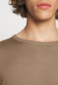 Brauner gerippter Strickpullover mit Rundhalsausschnitt. Nahaufnahme, die Textur und Farbe hervorhebt, mit glattem, figurbetontem Design.