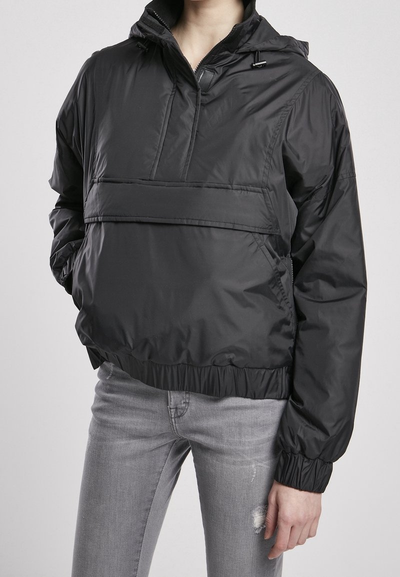 Veste-pull noire avec fermeture éclair à l'avant, poignets et ourlet élastiques. Fabriquée en matériau léger et brillant, dotée d'une capuche et d'une poche plaquée.