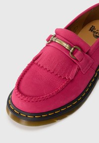 Pink leather loafer with fringe detail, brass hardware accent, stitched trim, and contrasting yellow stitching on a black sole.