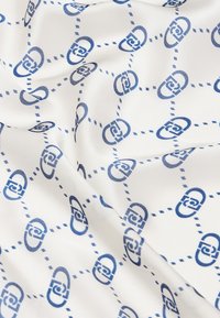 Tessuto di seta stampato con un design geometrico, caratterizzato da forme blu collegate su uno sfondo bianco, accentuato da linee punteggiate.