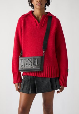 Maglione rosso lavorato a maglia con colletto, abbinato a una borsa rettangolare nera con logo in rilievo e tracolla regolabile, e una gonna plissettata a quadri.