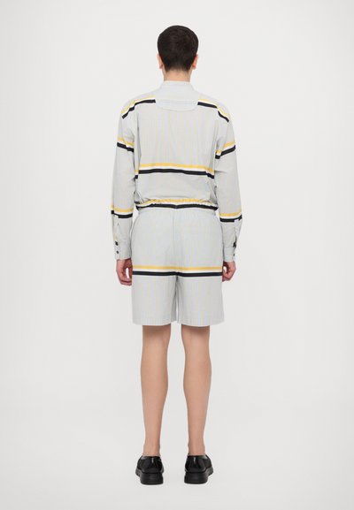 Blå og hvit stripete skjorte med gule og svarte detaljer, kombinert med matchende shorts; knappestenging, elastisk midjebånd og lett stoff.