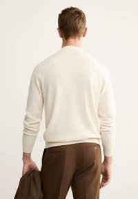 Maglione color crema con colletto rotondo, polsini e orlo a costine, abbinato a pantaloni marroni con due tasche posteriori e bottoni.