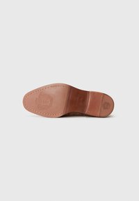 Suela de zapato de cuero con un acabado marrón suave, que presenta un logotipo decorativo en relieve, bordes cosidos y un diseño de punta redondeada.