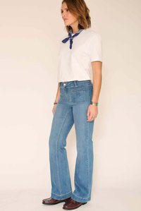 Jean flare bleu clair à taille haute, avec poches avant et arrière. Associé à un t-shirt blanc et un bandana bleu.