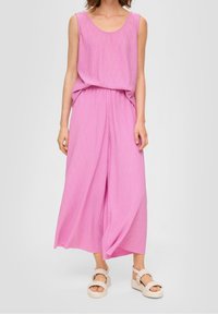 Růžový bezramínkový overal s volným střihem, nařaseným pasem a širokými nohavicemi. Look doplňují béžové platformové sandály.