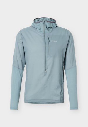 Hele sinine Patagonia kapuutsiga jakk, millel on pikad varrukad, poollukuga ees ja lukuga rinnatasku valgel taustal.