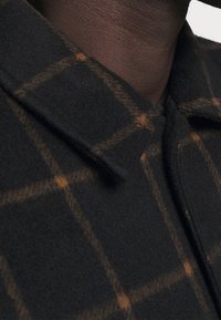 Kabát z vlněné směsi s černobrowným kostkovaným vzorem, s špičatým límcem a měkkou texturou, navržený pro teplo a pohodlí.