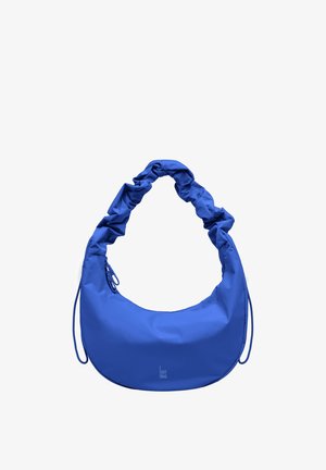 Blauwe tas in halve maanvorm met gerimpelde handgreep en klein "GOT BAG"-logo onderaan in het midden op een witte achtergrond.
