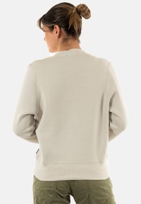 Sudadera de color beige claro con cuello redondo, mangas largas y un corte relajado. Textura suave con un bolsillo lateral discreto.