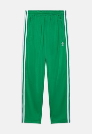 Zelené sportovní kalhoty vyrobené z hladkého materiálu, s bílými postranními pruhy, elastickým pasem a kapsami na zip. Přítomné logo Adidas.
