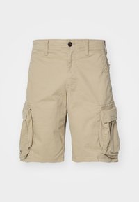 Short cargo beige avec bouton à l'avant, passants de ceinture et grandes poches à rabat de chaque côté sur un fond uni.