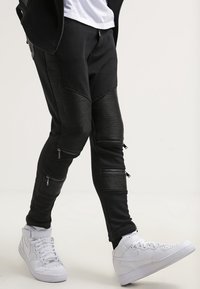 Svarta joggerbyxor med ribbad textur och dragkedjefickor, kombinerade med vita högklackade sneakers. Designen har en slim fit och kontrasterande paneler.