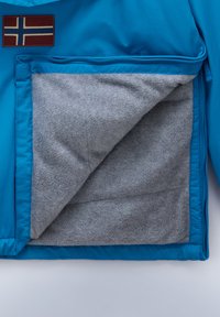 Giacca blu con una tasca con zip foderata in pile grigio, che presenta un'esterno liscio e lucido e un'emblema che ricorda una bandiera.