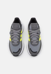 Sportovní tenisky v šedé barvě s žlutými pruhy. Síťovina a syntetický svršek, zaoblená špička, design na šněrování, polstrovaný límec a bílá gumová podešev.