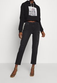 Sudadera negra recortada con un estampado gráfico, combinada con jeans negros de cintura alta que presentan detalles desgastados y un corte recto, llevados con sandalias de tacón.