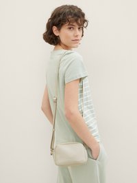 Borsa a tracolla verde chiaro con finitura testurizzata, dotata di chiusura con zip e una lunga tracolla regolabile, abbinata a una maglietta e pantaloni a righe.