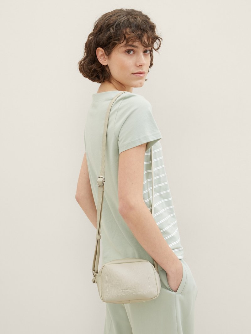 Borsa a tracolla verde chiaro con finitura testurizzata, dotata di chiusura con zip e una lunga tracolla regolabile, abbinata a una maglietta e pantaloni a righe.