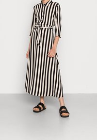 Czarna i kremowa w paski midi sukienka z rękawami do 3/4, guziki z przodu, przewiązany w talii i zwiewna sylwetka, w połączeniu z czarnymi sandałami.