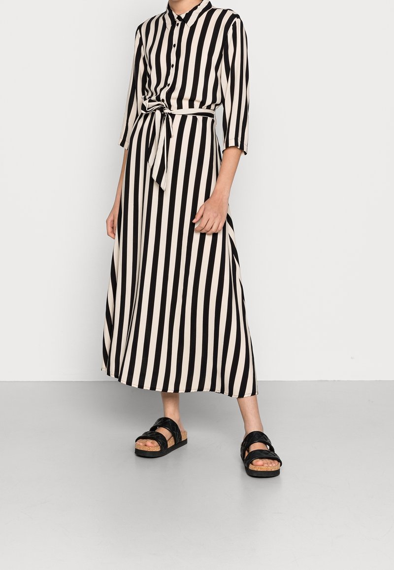 Czarna i kremowa w paski midi sukienka z rękawami do 3/4, guziki z przodu, przewiązany w talii i zwiewna sylwetka, w połączeniu z czarnymi sandałami.