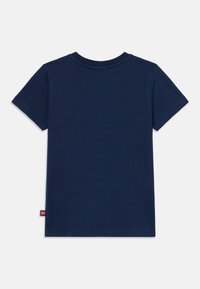 T-shirt en coton bleu marine à manches courtes, col rond, avec une petite étiquette logo rouge sur le bas à gauche. Texture lisse, design simple.