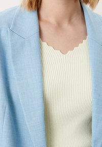 Světlomodrý blazer s ostře řezanými klopami, spárovaný s krémovým žebrovaným topem se scalloped výstřihem. Důraz na měkké textury a pastelové barvy.