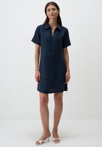 Robe bleu marine à manches courtes avec un col et une fermeture éclair à l'avant. Fabriquée en tissu léger, elle a une coupe droite et une longueur au genou.