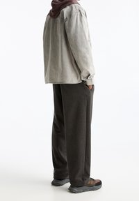 Szara koszula dżinsowa z burgundowym kołnierzykiem, w zestawieniu z ciemnymi spodniami i wielokolorowymi butami trekkingowymi, prezentująca luźny krój i boczne kieszenie.