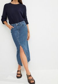 Gonna a matita in denim di colore azzurro chiaro con uno spacco laterale alto fino alla coscia e design classico a cinque tasche. Abbinata a una blusa blu navy e sandali marroni.