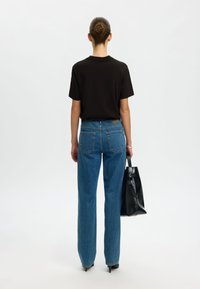 Juodas trumpomis rankovėmis marškinėliai derinami su aukštu juosmeniu mėlynais džinsais. Modelis laiko juodą rankinę ir vilki smailiais juodais batais.