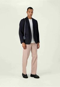 Blazer marine sur un t-shirt blanc, pantalon rose clair et chaussures noires ; comprend un sac bandoulière simple. Textures lisses et coupe ajustée.