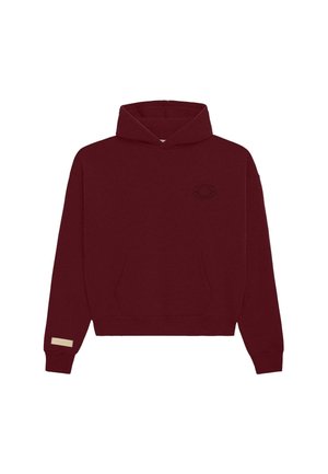 Burgunderfarbener Cropped-Hoodie mit frontaler Kängurutasche, kleinem schwarzem besticktem Runddesign auf der linken Brust und beigem Etikett am Bündchen des linken Ärmels.