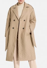 Abrigo beige acolchado con diseño de doble botonadura, solapas grandes y bolsillos laterales. Presenta un patrón texturizado y botones oscuros.