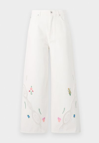 Pantalons larges blancs en denim avec broderie florale et dentelle le long de l'ourlet. Dispose de cinq poches et d'une fermeture à bouton à l'avant.