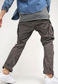 Pantalon cargo en tissu gris foncé avec une coupe décontractée, doté de poches latérales et de revers retroussés, associé à des baskets blanches.