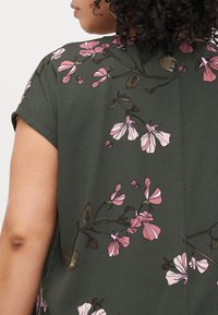 Dark green fabric top featuring pink floral patterns with short sleeves and a relaxed fit; detailed with leaves and accent embroidery.