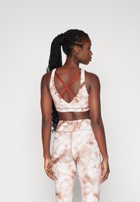 Smeđa i bež tie-dye sportska bralette sa ukrštenim trakama i odgovarajućim tajicama. Teksturirana, rastezljiva tkanina, dizajnirana za aktivno nošenje.