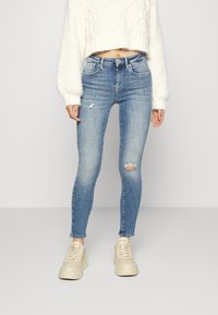 Smala jeans i ljusblå denim med slitna knän, kombinerat med en vit fluffig tröja och krämfärgad sneakers, vilket skapar en avslappnad look.