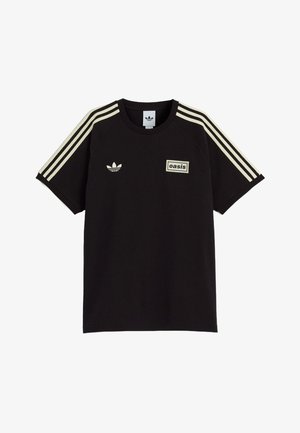 T-shirt nera Adidas con strisce crema sulle maniche, logo trefoil Adidas sul petto a sinistra e patch "oasis" sul petto a destra.