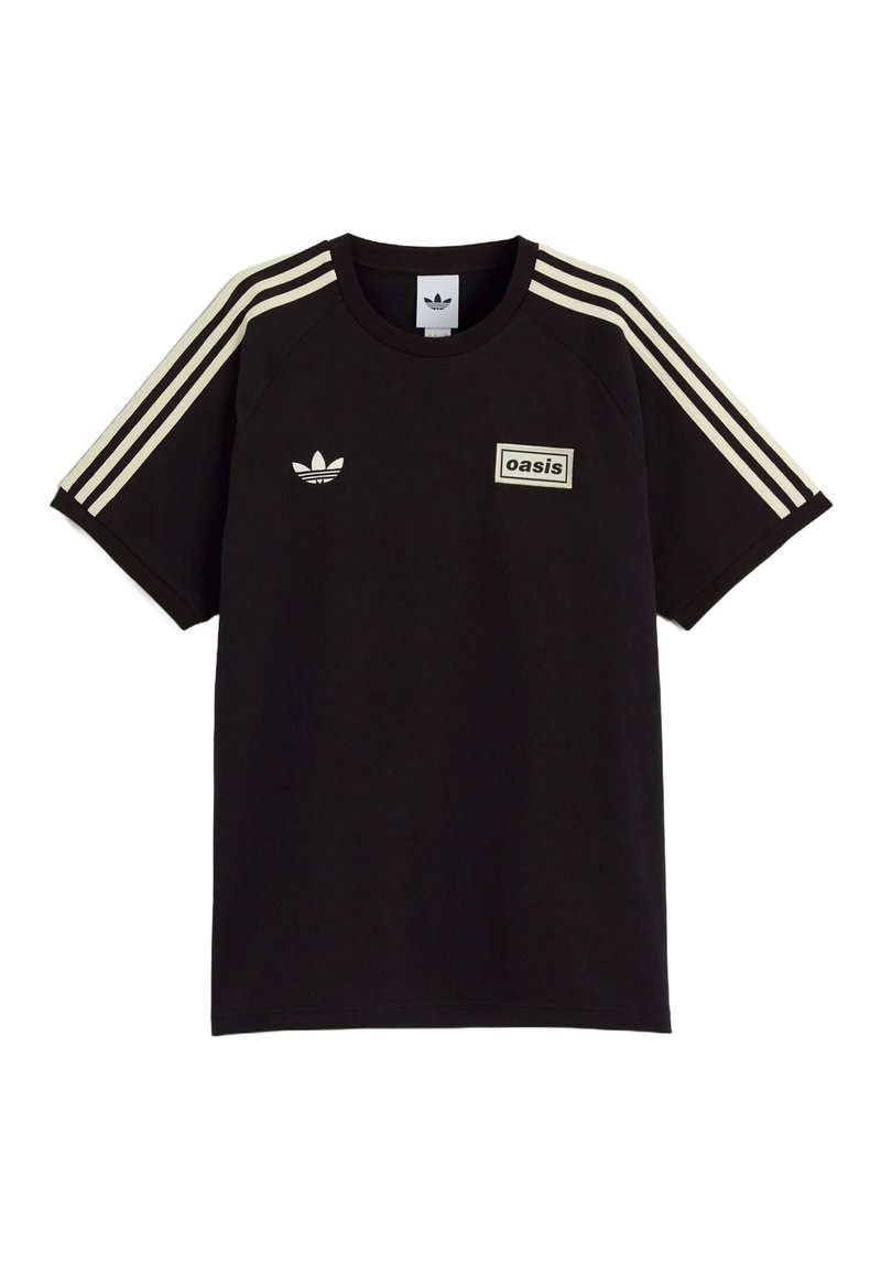 T-shirt nera Adidas con strisce crema sulle maniche, logo trefoil Adidas sul petto a sinistra e patch "oasis" sul petto a destra.