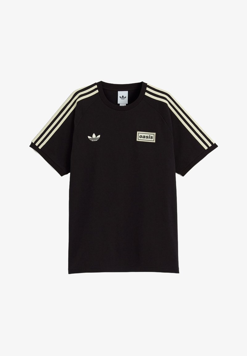 Zwarte Adidas T-shirt met crèmekleurige strepen op de mouwen, Adidas trefoil logo op de linkerkant van de borst en een "oasis" patch op de rechterkant van de borst.