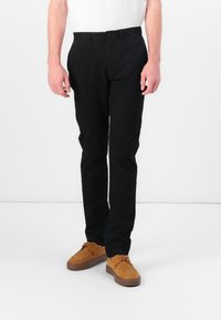Sorte bomullsbukser med flat front og slim fit. Kombinert med brune semskede sko med snøring og gummisåler. Enkel, ren design.