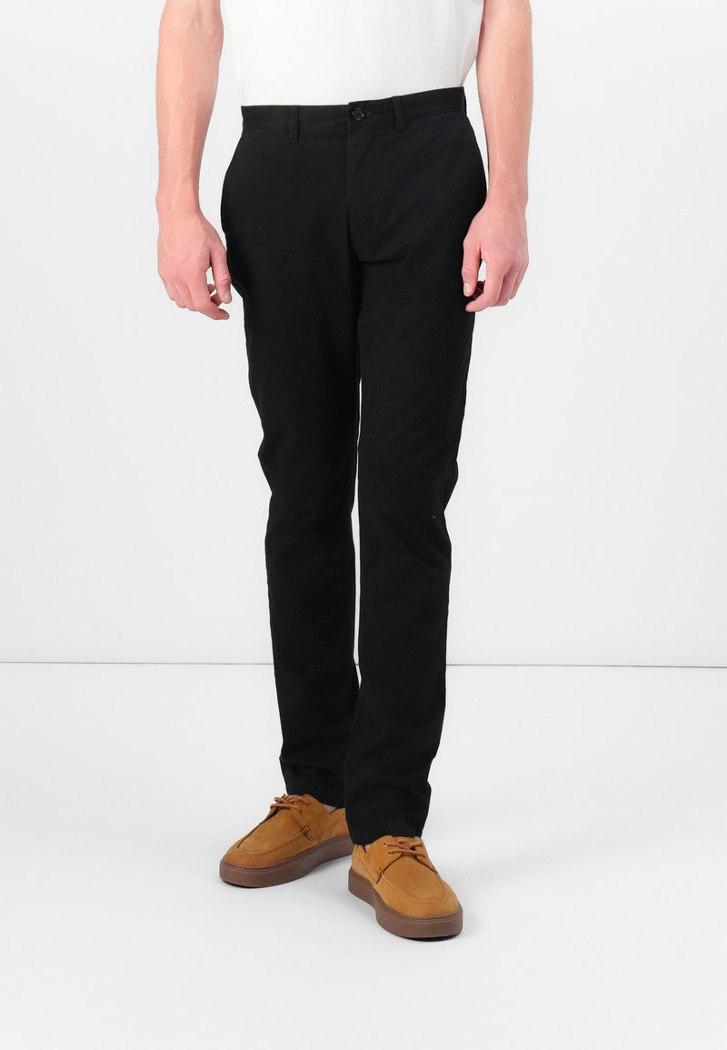 Sorte bomullsbukser med flat front og slim fit. Kombinert med brune semskede sko med snøring og gummisåler. Enkel, ren design.