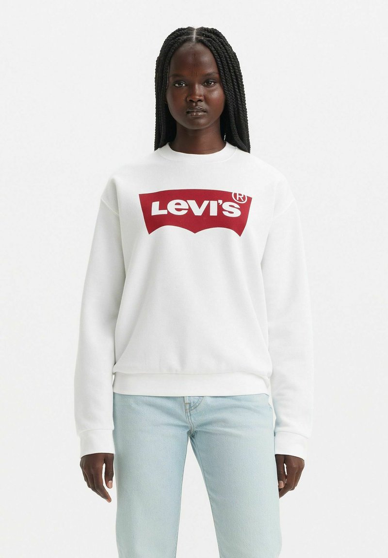 Vit sweatshirt med röd Levi's-logotyp, rund halsringning, ribbade ärmslut och nederkant. Bärs med ljusblå jeans. Enkelt och avslappnat design.